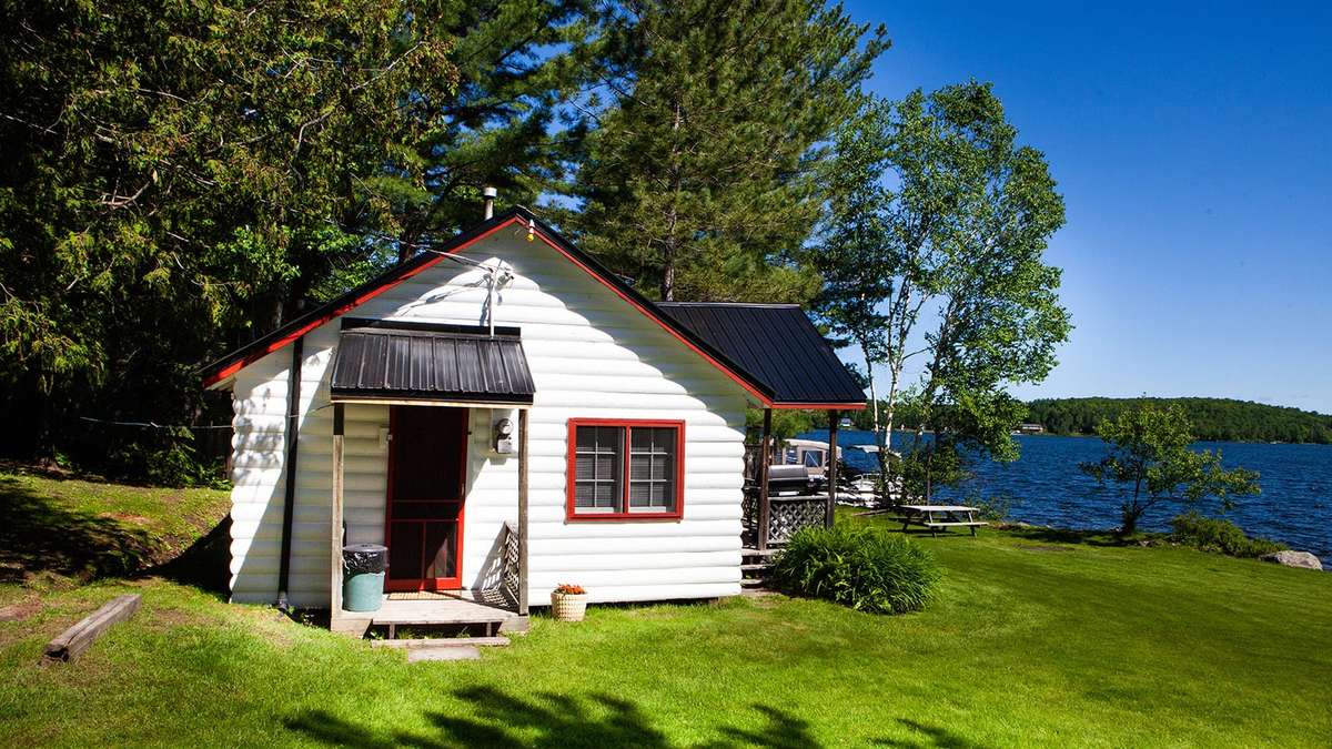 Loon Landing, a white cottage with red trim, with the lake behind it