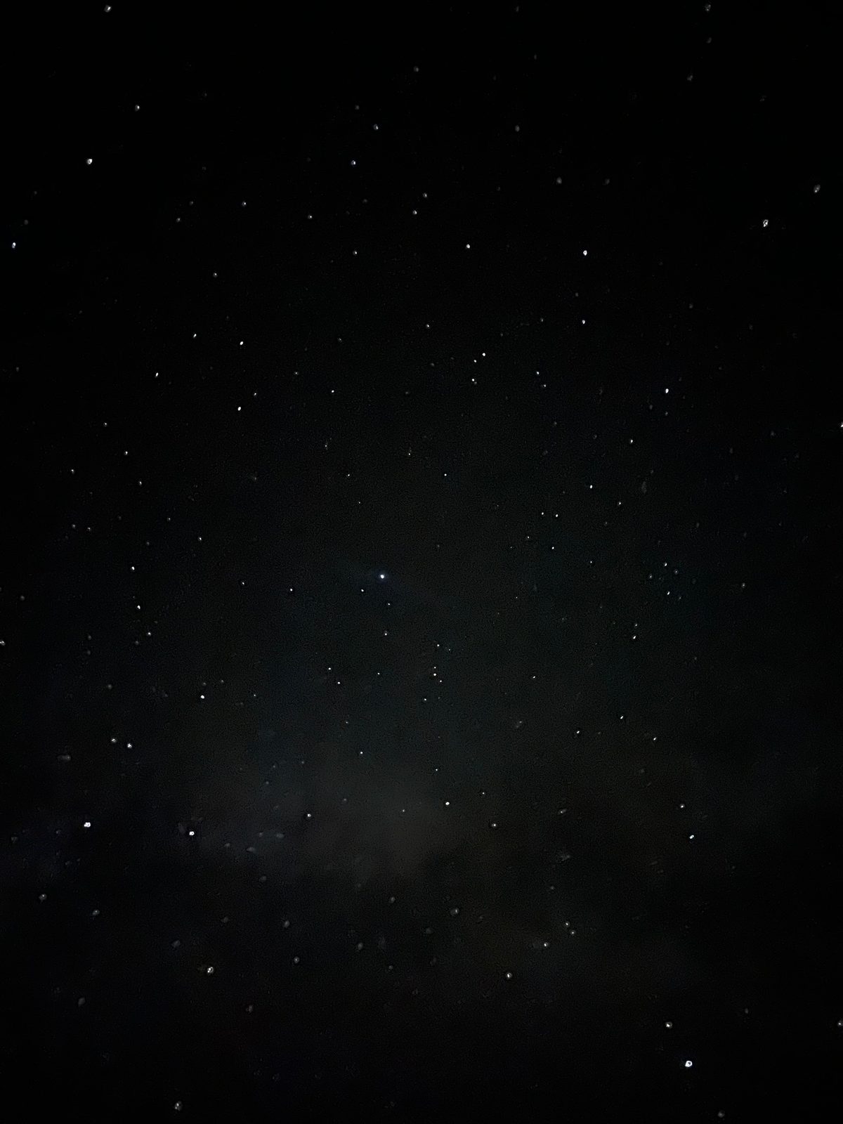 A dark night sky scattered with stars, one bright star near the middle and a faint haze of light low in the sky